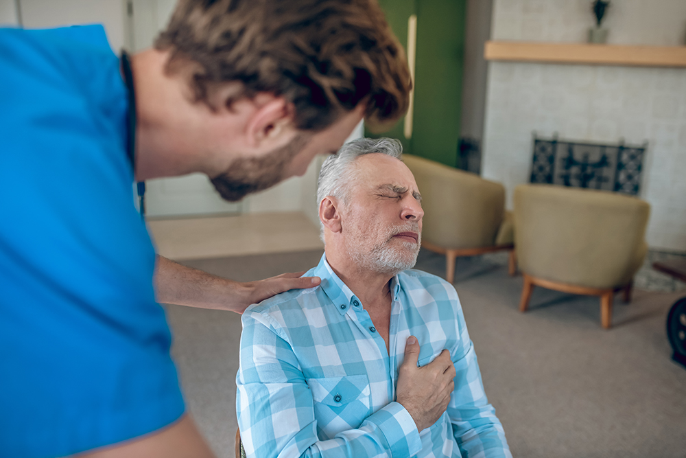 Dark-haired doctor bending towards a mature Caucasian man with a chest pain