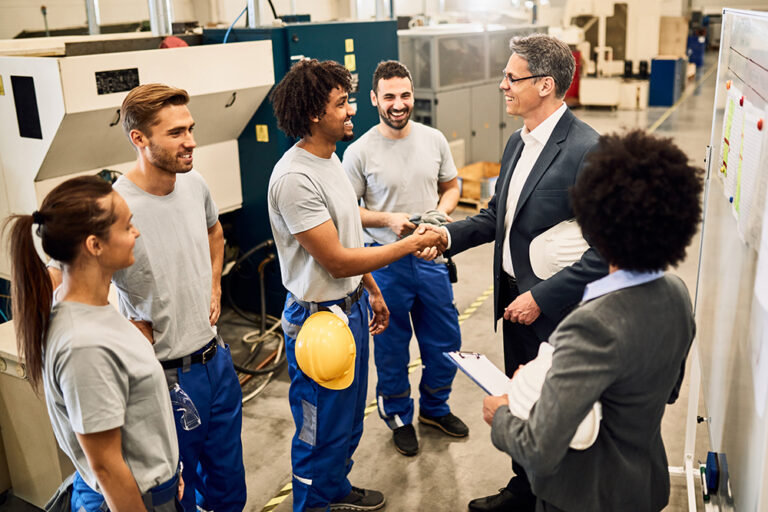 Happy corporate manager shaking hands with black worker after staff meeting in a factory.