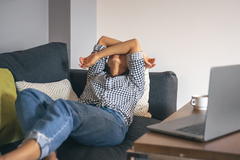 Tired from work, a young woman with a laptop lies on the couch.